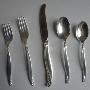 May include: A set of five silver-plated cutlery pieces, including a knife, fork, and three spoons. The handles feature a delicate floral design.