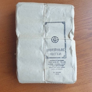 May include: A brown paper package tied with string. The package is labeled "ШВЕЙНЫЕ НИТКИ" (Sewing Threads) and includes the text "хлопчатобумажные ГОСТ 6309-87 35x58. Комбинат Советская звезда 1 Сорт МАТОВЫЕ намотка 171г. отбеленные 10 БОБИН" (Cotton ГОСТ 6309-87 35x58. Soviet Star Combine 1 Grade MATTE winding 171g. bleached 10 SPOOLS).