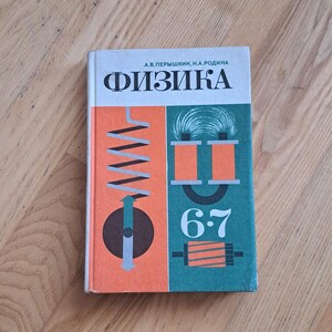 Op de afbeelding: Een leerboek getiteld "Fysica" in het Russisch, met de titel in grote, vette letters. De omslag heeft geometrische ontwerpen in oranje en blauwgroen, met de cijfers "6-7". Het boek ligt op een houten oppervlak.