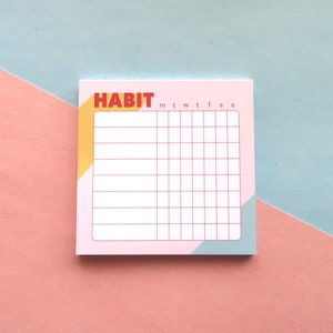 May include: A pink habit tracker notepad with a grid for tracking habits. The word "HABIT" is in red block letters at the top, with the days of the week abbreviated below. The notepad has a geometric design with yellow and blue accents.