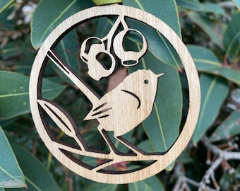 Könnte beinhalten: Ein Holz-Anhänger mit einem Laser-geschnittenen Design eines Vogels, der auf einem Ast mit Beeren sitzt. Der Anhänger ist in einem natürlichen Holzton lackiert und hat ein grünes Band zum Aufhängen.