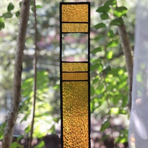 May include: A stained glass panel with a vertical design. The panel is made of multiple pieces of glass in shades of yellow and gold. The glass has a textured surface.