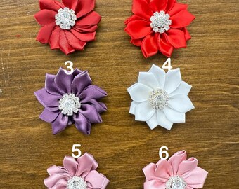May include: Six satin fabric flower embellishments with rhinestone centers. The flowers are in red, purple, white, and pink.