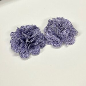 May include: Two purple burlap flowers with a ruffled texture.