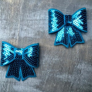 May include: Two turquoise blue sequined bow patches. The bows are made of sequins and have a shiny finish.
