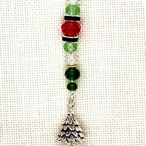 May include: A silver charm with a green, red, and clear crystal bead design. The charm is attached to a silver lobster clasp and has a small silver pine tree charm at the bottom.