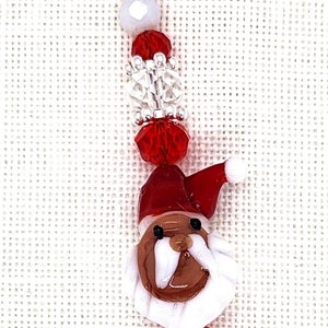 May include: A red and white beaded keychain with a glass Santa Claus charm and a silver charm that says "Merry Christmas".