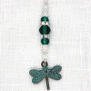 May include: A silver charm with a green dragonfly pendant and green crystal beads. The charm is attached to a silver lobster clasp.