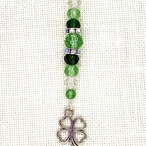 May include: A silver charm with a green crystal bead and a four-leaf clover charm. The charm is attached to a silver clasp.