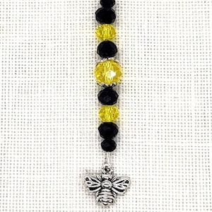 May include: A silver charm with a black and yellow crystal bead design and a silver bee charm.