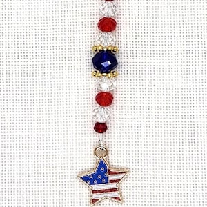 May include: A patriotic charm featuring a silver clasp, red and clear beads, a blue bead, and a gold star charm with a red, white, and blue design. The charm is designed with a patriotic theme.