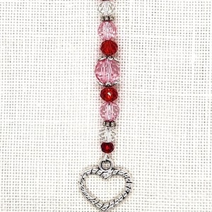 May include: A silver heart charm with a beaded chain attached to a silver lobster clasp. The beads are red, pink, and clear.