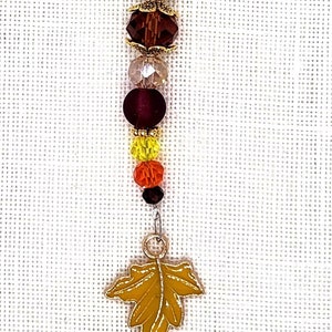 May include: A silver charm with a gold leaf charm and a beaded chain with red, orange, yellow, and brown beads.
