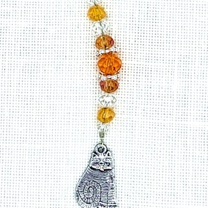May include: A silver charm of a cat with orange and clear glass beads on a silver wire.
