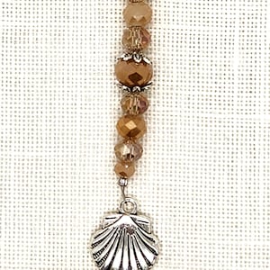 May include: A brown and silver beaded charm with a seashell pendant. The beads are faceted and have a shimmery finish.