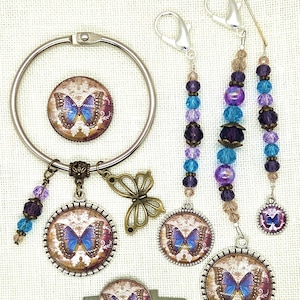 May include: A collection of butterfly-themed accessories, including a round keychain, beaded charms, and a key. The items feature a blue butterfly design on a patterned background, with silver and bronze metal accents.