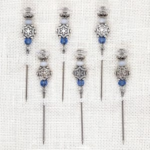 May include: Six silver snowflake cocktail picks with blue and white beads. The picks are made of metal and have a pointed end.