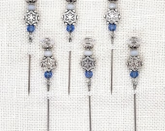 May include: Six silver snowflake cocktail picks with blue and white beads. The picks are made of metal and have a pointed end.