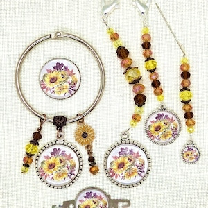 May include: A collection of sunflower-themed accessories, including a large ring, charms, and beaded accents. The charms feature a sunflower design with yellow, purple, and brown hues. The accessories are set against a white background.