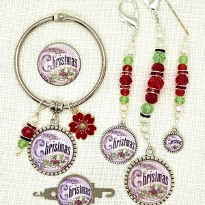 May include: A collection of Christmas-themed accessories, including a binder ring, charms, and stitch markers. The charms and stitch markers feature the word "Christmas" in a decorative font, with red, green, and white bead accents. A red flower charm is also included.