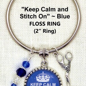 Puede incluir: Un anillo de hilo plateado con un dije azul y plateado. El dije tiene el texto "Keep Calm and Stitch On!" y una corona. Tambi&eacute;n se adjuntan un dije de tijeras y cuentas azules. El anillo tiene 5,08 cm de di&aacute;metro.
