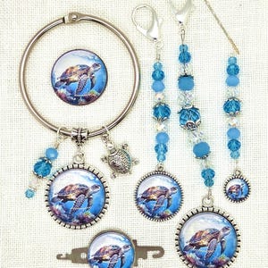 May include: A collection of sea turtle-themed accessories, including a round keychain, key fobs, and beaded charms. The charms feature a detailed image of a sea turtle swimming in the ocean, with blue and turquoise accents.