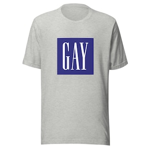 Może przedstawiać: Szara koszulka z niebieskim kwadratem, na którym widnieje napis "GAY" białymi literami.