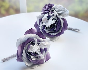 May include: Paper flower bouquets with purple, silver, and white petals. Each rose features a silver dragon embellishment. The stems are wrapped in a matching silver material. The flowers are arranged on a white surface.