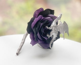 May include: A black and purple rose with a silver dragon perched on top. The rose is on a white surface.