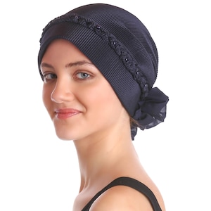 May include: A navy blue head covering with a ribbed texture and a decorative braided band. The head covering has a gathered design at the back and is made of a soft, draping fabric. The head covering is designed to be worn on the head.