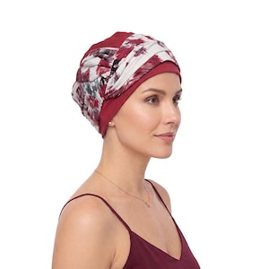 May include: A head wrap featuring a solid deep red base colour with a contrasting overlay of white fabric patterned with abstract dark red and black brushstroke designs. The head covering is styled with gathered pleats and a twisted knot detail.