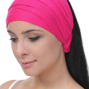 May include: A bright pink headband made of soft fabric. The headband is folded and tied at the back of the head.
