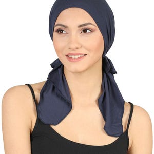 Può includere: Un copricapo blu navy a tinta unita realizzato in tessuto morbido che copre la sommità della testa e presenta due lunghi lacci rettangolari che ricadono su entrambi i lati del collo. Il copricapo è realizzato con una finitura liscia e opaca.
