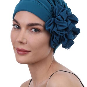 Op de afbeelding: Tealkleurige hoofdbedekking met een groot, gerimpeld bloemaccent. De haarwikkel heeft een geplooid ontwerp en is gemaakt van een zachte stof. De bloem is gemaakt van hetzelfde materiaal en voegt een decoratief tintje toe. Dit accessoire is stijlvol.