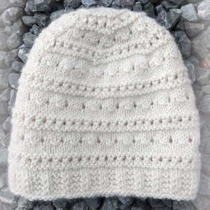 Puede incluir: Un gorro de punto blanco con un delicado patrón de puntadas. El gorro está hecho de un hilo suave y esponjoso y tiene un diseño simple y clásico.