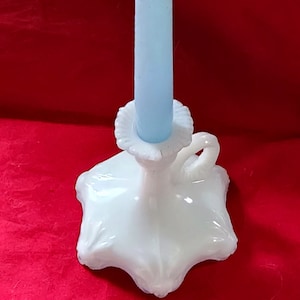 May include: White milk glass candlestick with a fluted base and a handle. A light blue candle is in the holder.