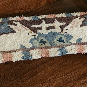 May include: A small, rectangular footstool with a hand-woven rug top featuring a colorful geometric pattern with two white rabbits. The footstool has two black metal legs.