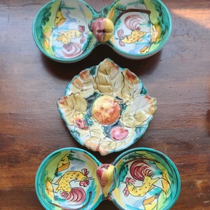 May include: Three ceramic serving dishes with colorful hand-painted designs. Two of the dishes are divided in half and feature roosters and fruit. The third dish is round and features a fruit design with leaves.