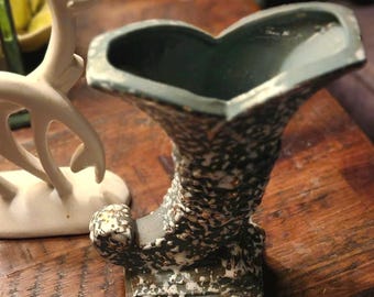 May include: A green and white ceramic vase with a speckled glaze. The vase is shaped like a boot and has a wide opening at the top.