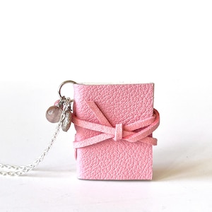 May include: A pink leather journal with a silver chain and charms. The journal is tied with a pink ribbon and has a textured surface.