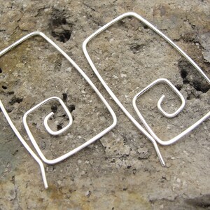 May include: A pair of silver earrings with a spiral design. The earrings are made of thin wire and have a simple, modern look.