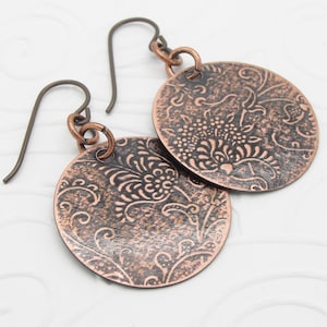 May include: A pair of copper earrings with a distressed finish and a floral pattern. The earrings are round and have a hook closure.