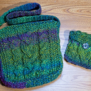 Könnte beinhalten: Eine grüne, blaue und violette gestrickte Tragetasche mit einer passenden kleineren gestrickten Tasche. Die Tasche hat einen dekorativen Knopf.