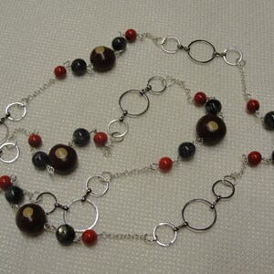 May include: A silver chain necklace with red, black, and brown beads. The necklace features a variety of circular silver links.