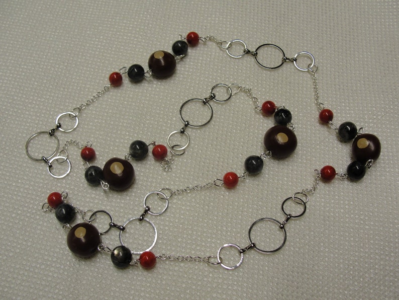 May include: A silver chain necklace with red, black, and brown beads. The necklace features a variety of circular silver links.