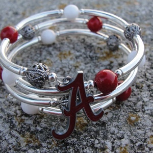 May include: Silver bangle bracelet with red and white beads and a silver charm with the letter 'A' in red enamel.