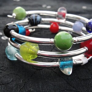 May include: A silver bangle bracelet with multiple layers of colorful glass beads. The beads are green, red, blue, black, and white.