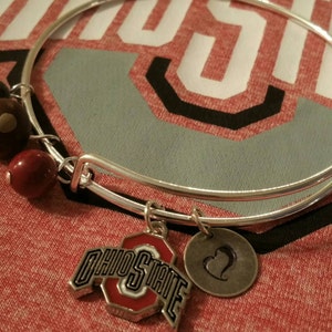 Könnte beinhalten: Ein silbernes Armband mit einem roten, weißen und schwarzen Ohio State-Anhänger, einem silbernen Herz-Anhänger und braunen, roten und grauen Perlen.