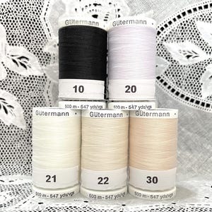 May include: Five spools of Gütermann sewing thread arranged in a pyramid. The top row features black and white thread labeled 10 and 20. The bottom row includes three shades of cream and beige thread labeled 21, 22, and 30. Each spool contains 547 yards.