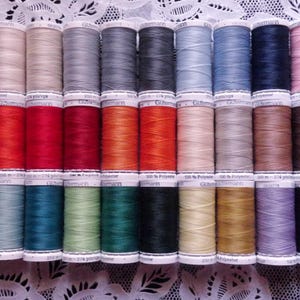 May include: A collection of colorful spools of Gutermann sewing thread. The spools are arranged in rows, showcasing a wide spectrum of colors, including black, white, pink, orange, red, green, blue, and brown. Each spool is labeled with text.